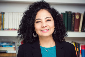 Photo of Rosa Cervantes, Counsellor in Psychology, sitting in front of a book case, smiling